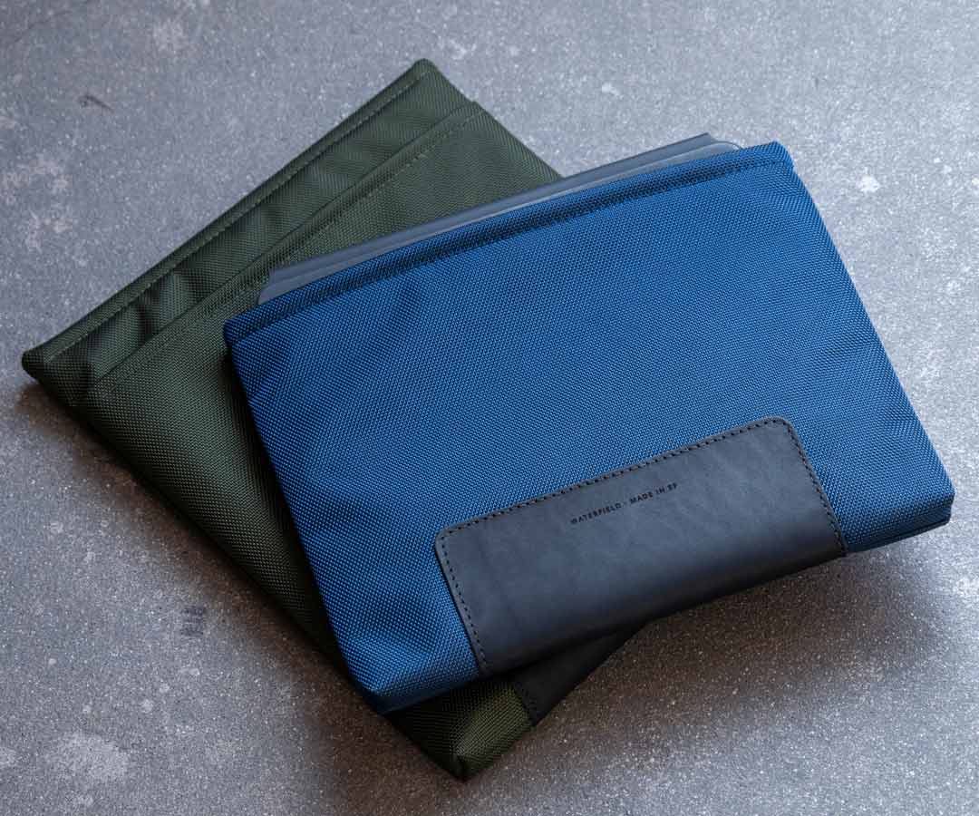 Blue and green padded sleeves stacked over iPad and tablet on grey surface