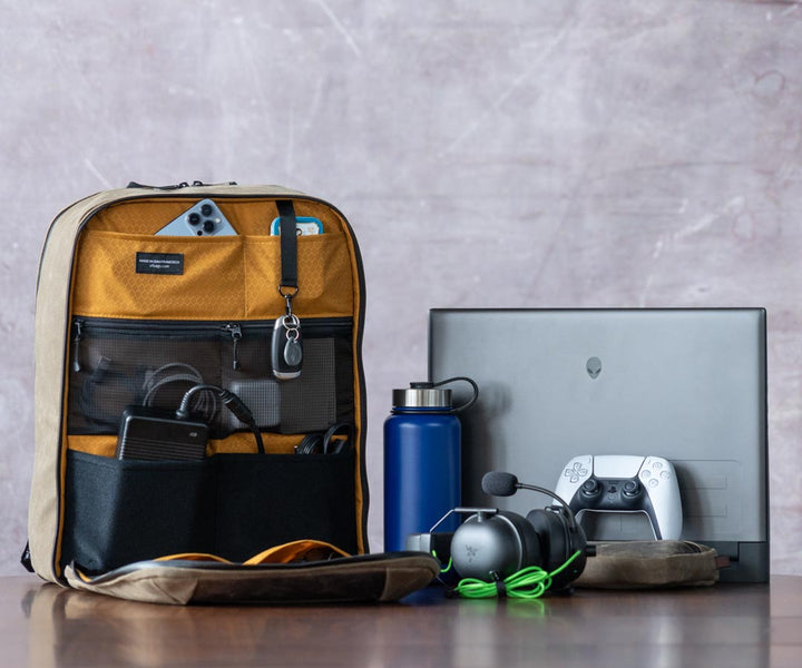 Open Tech Folio Tank backpack on table with accessories including laptop, controller, and water bottle